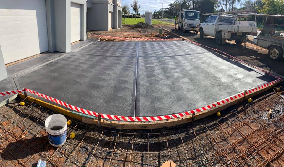A freshly poured garage apron behind hazard tape with utes parked on the street
