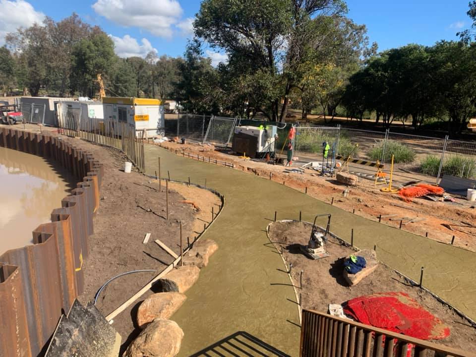 A wide poured base beside sheet piling on a creek-side civil site