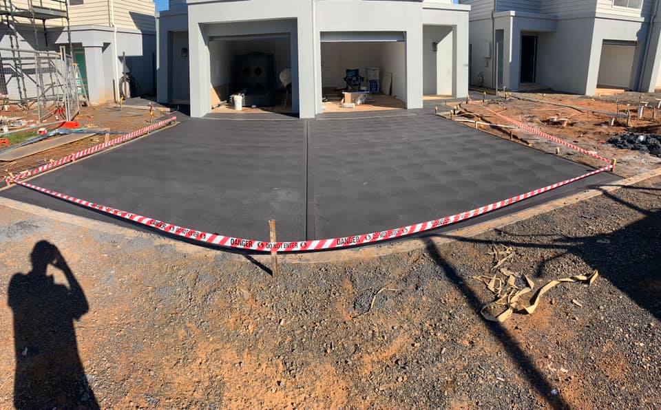 A freshly finished driveway slab in front of a new build behind hazard tape