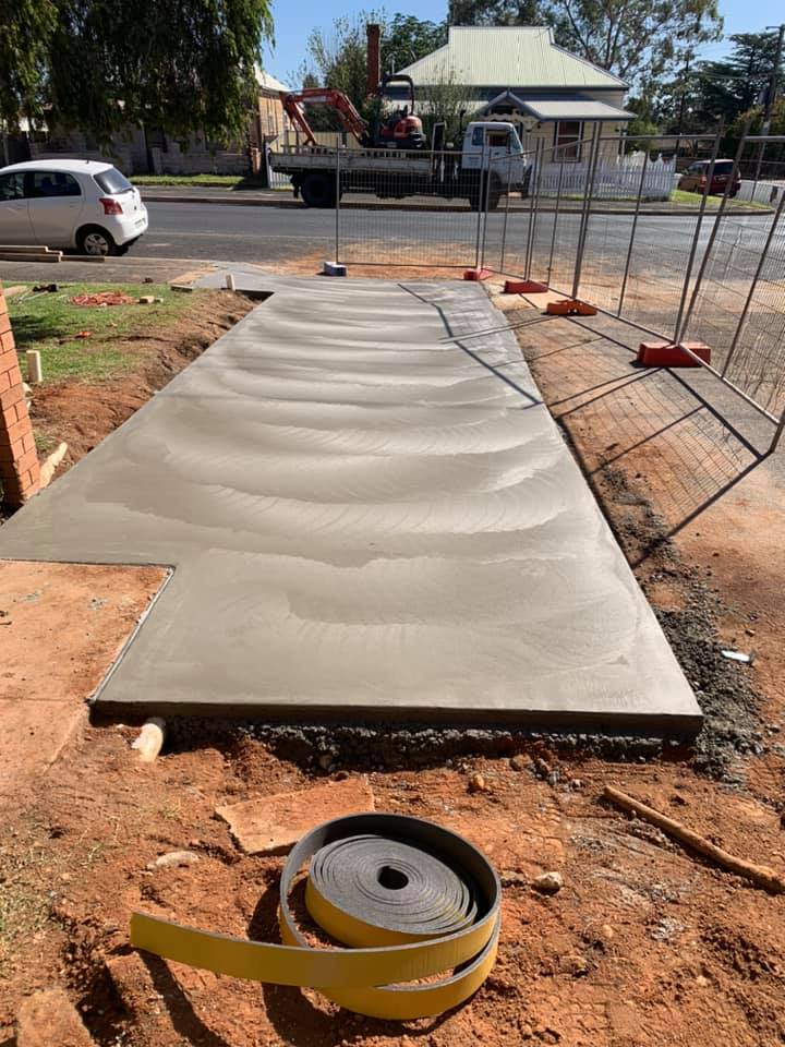 A broom-finished concrete pad sitting on cut red soil behind temporary fencing