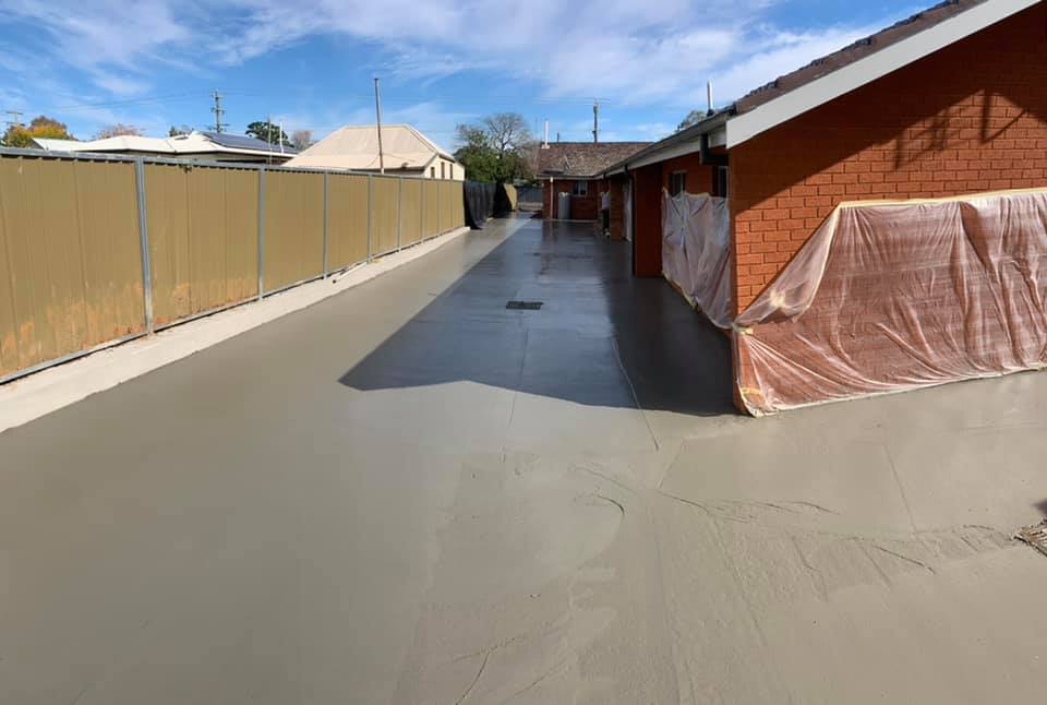 A concrete driveway poured between a brick building and a hoarding fence