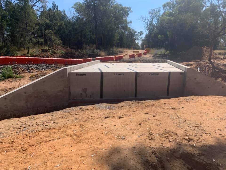 A row of precast box culverts bedded into a formed concrete channel in red soil