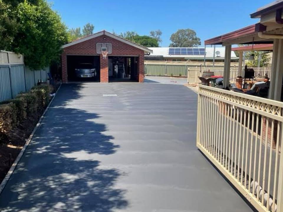 A concrete driveway running to a brick garage with a basketball ring above the door