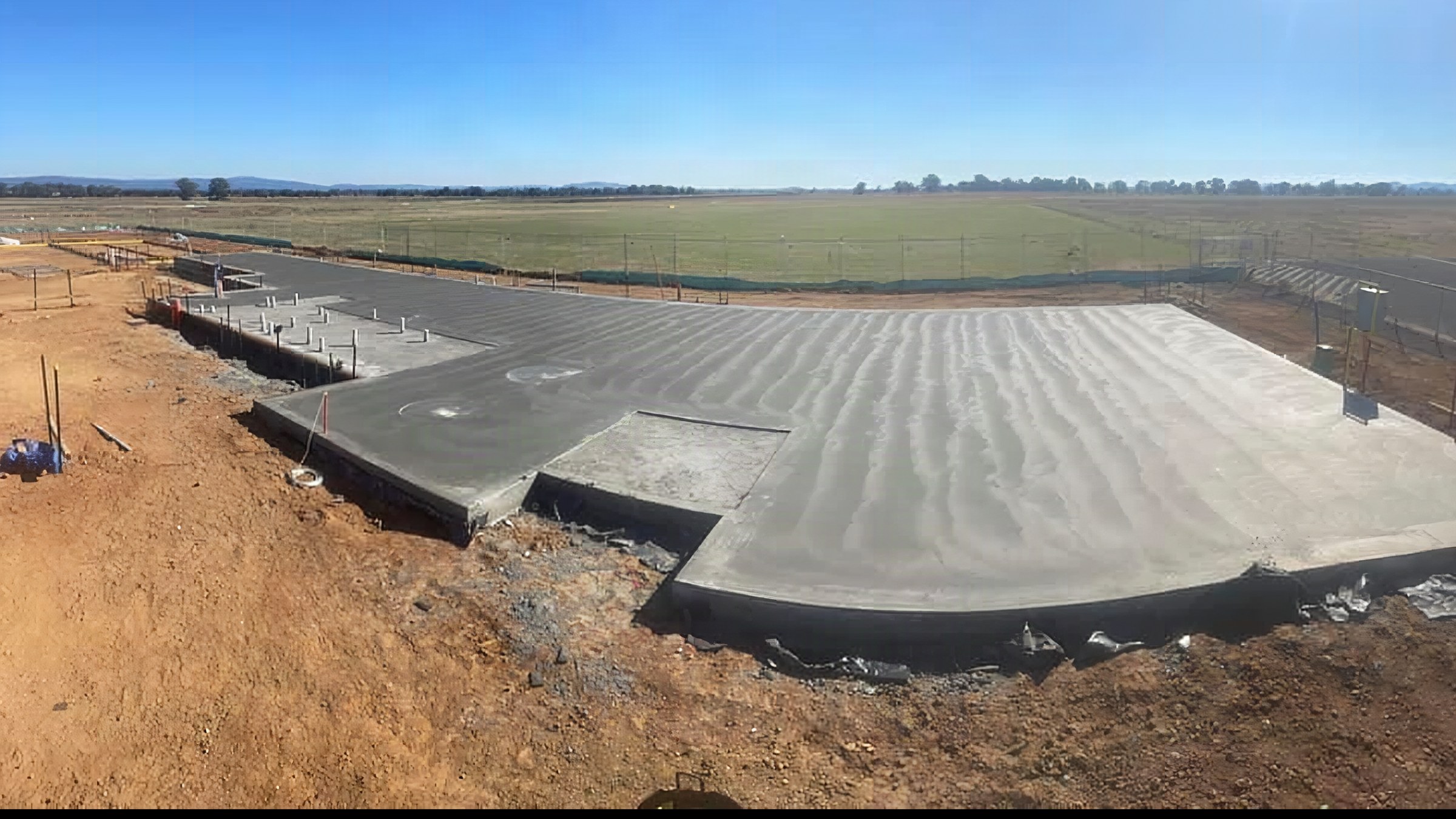 A broom-finished rural slab poured against cut red soil with paddocks behind