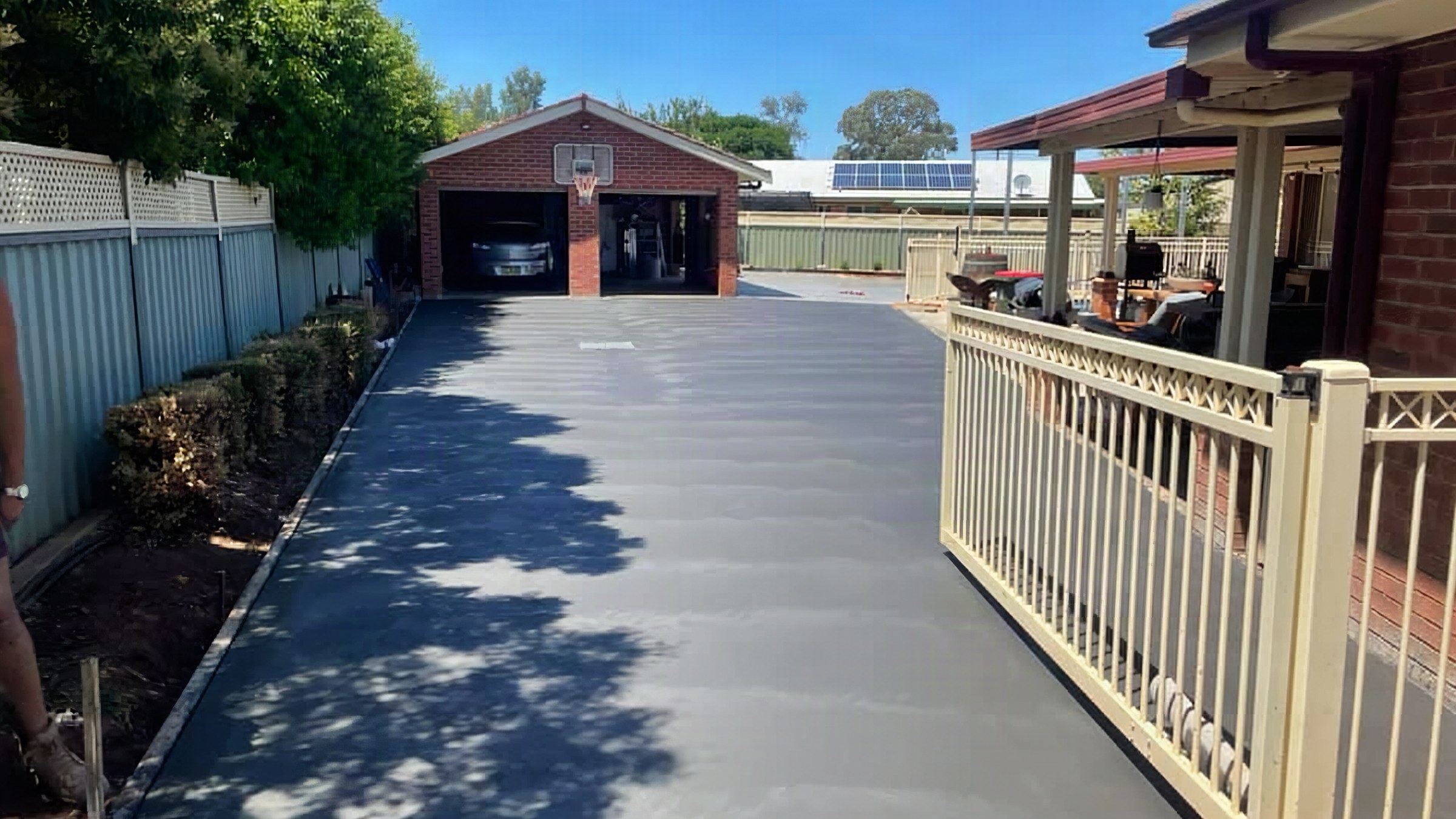 A wide concrete driveway beside a fenced verandah leading to a brick garage