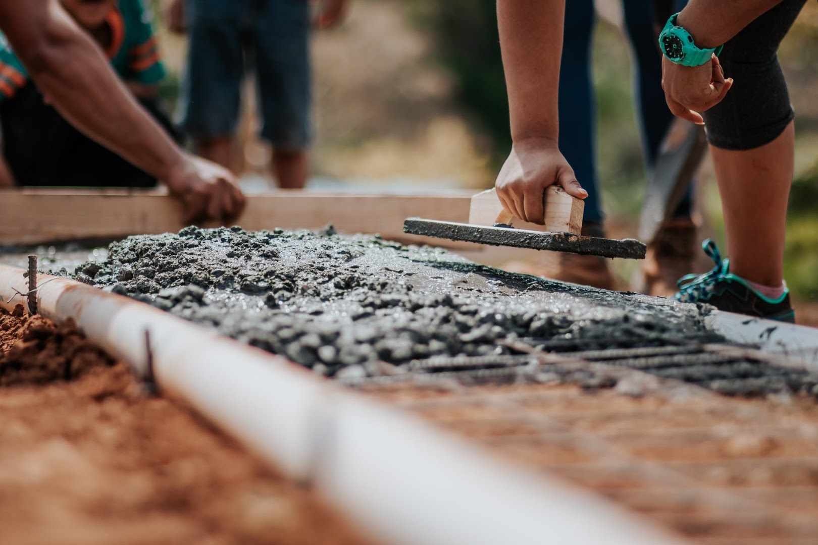 Hands working a screed board and float across freshly poured concrete beside a formed edge