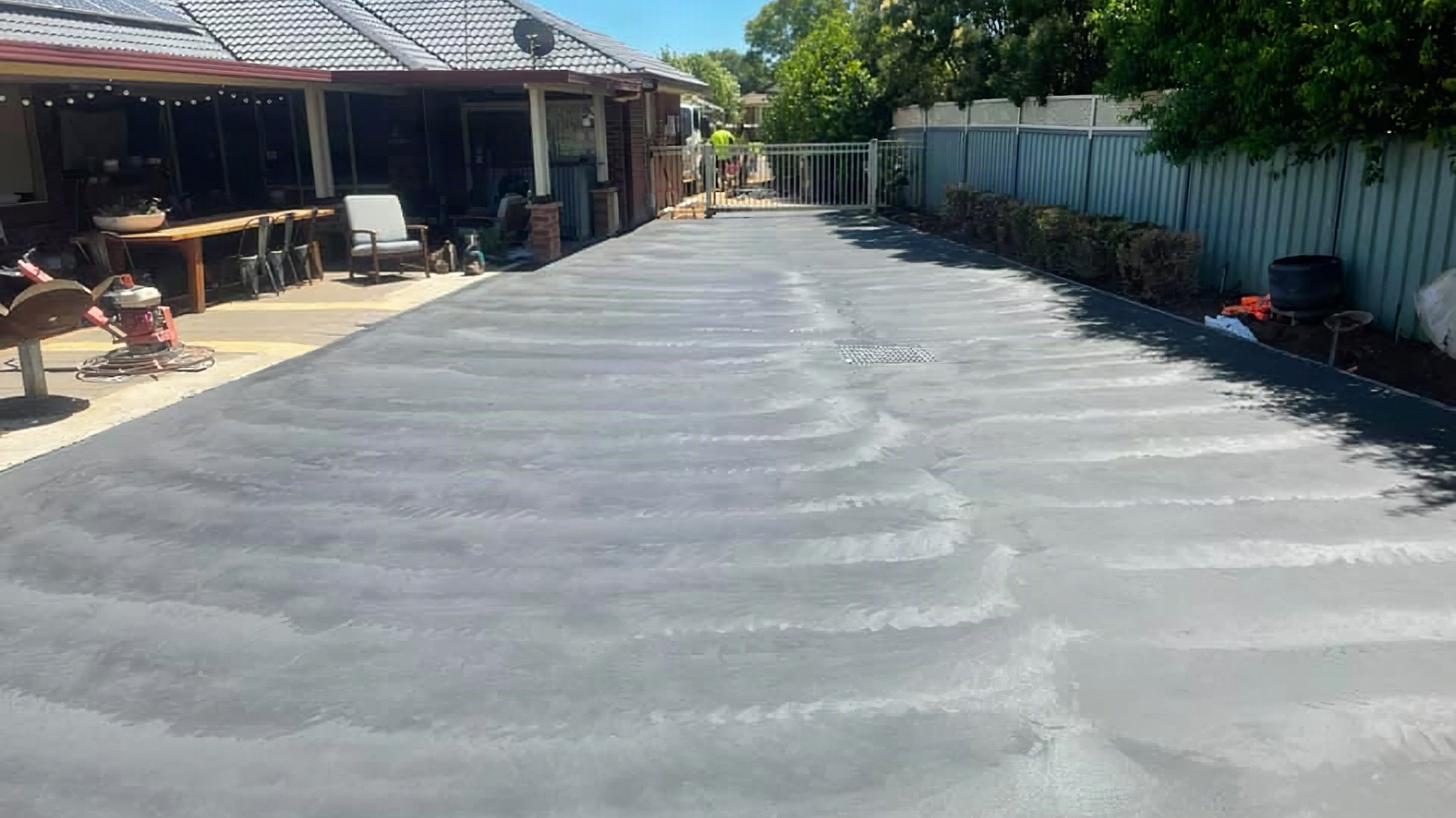 A freshly poured driveway running between a house and a colorbond fence