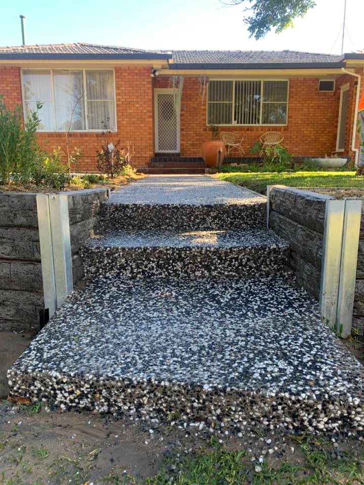 Exposed aggregate steps and a landing leading up to a brick home between retaining walls