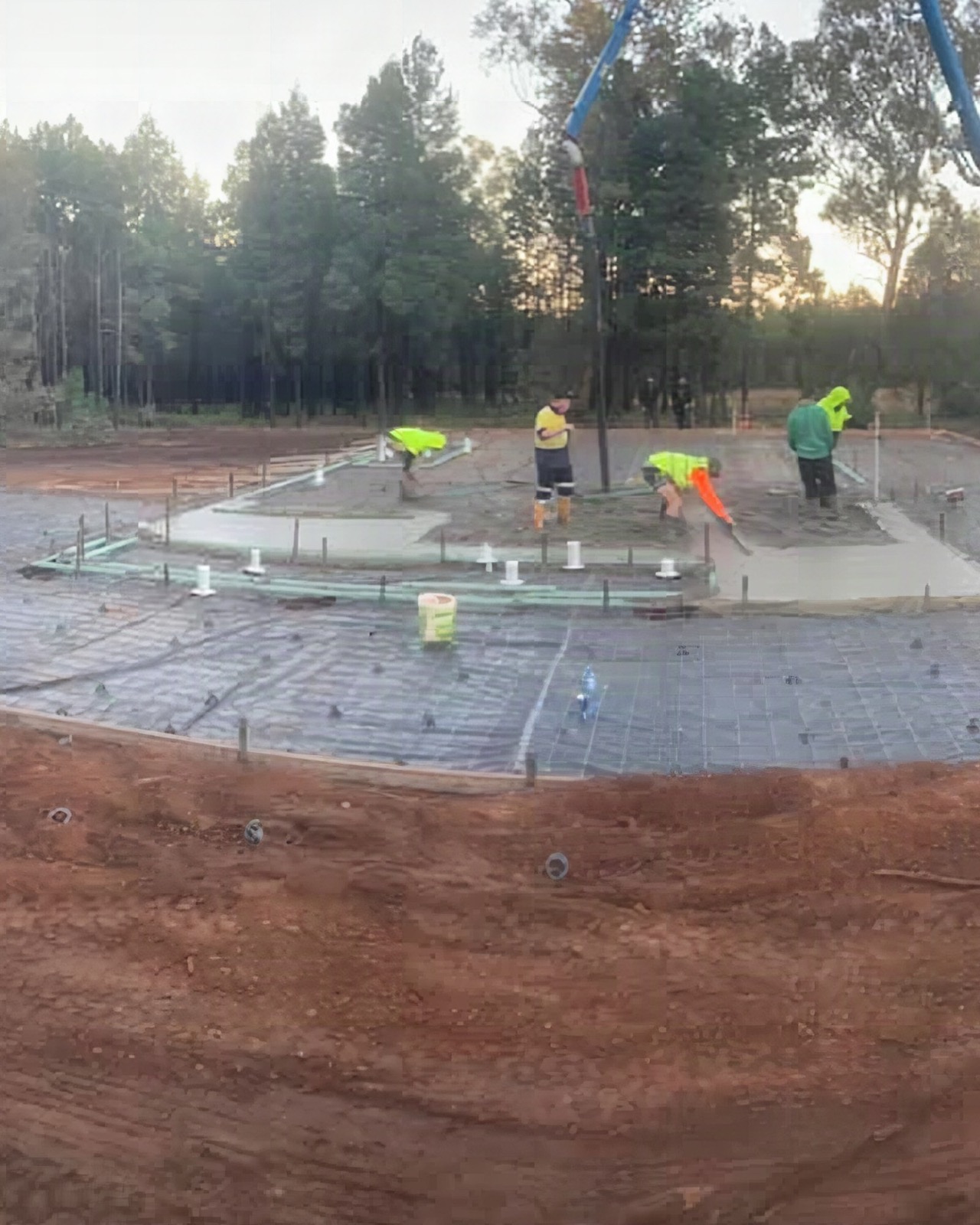 Three workers finishing a large slab on a cleared rural block with cut red soil around it