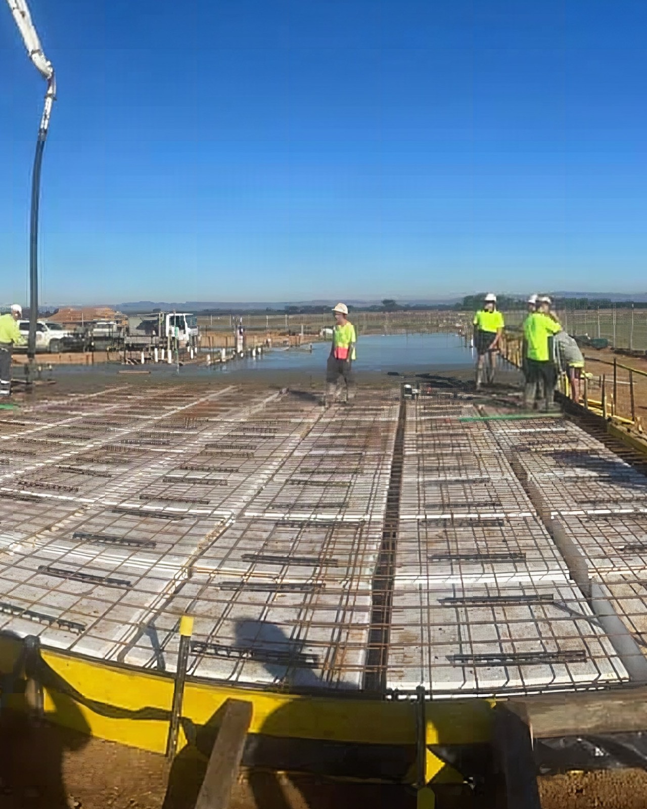 A crew standing on a large reinforced slab bed with the pump line in place