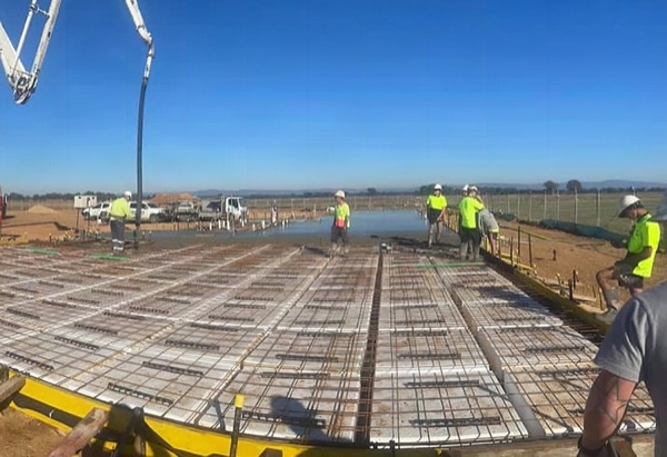 A crew standing on a large steel-fixed slab bed with the pump line overhead