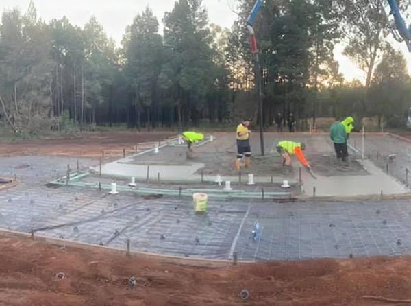 Workers finishing a large rural slab surrounded by cut red soil