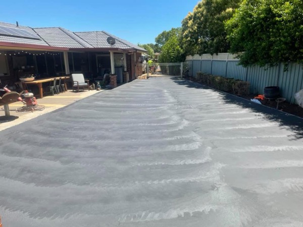 A freshly poured driveway running between a house and a colorbond fence