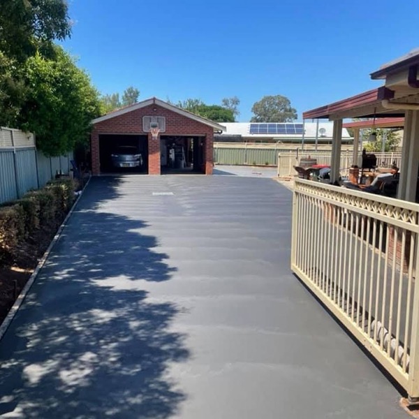A concrete driveway running to a brick garage with a basketball ring above the door