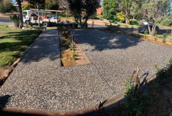 An exposed aggregate driveway curving past a garden bed