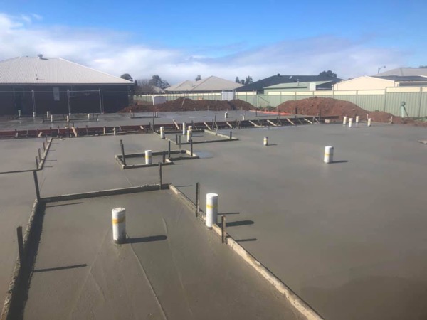 A poured slab with plumbing penetrations and starter bars standing proud