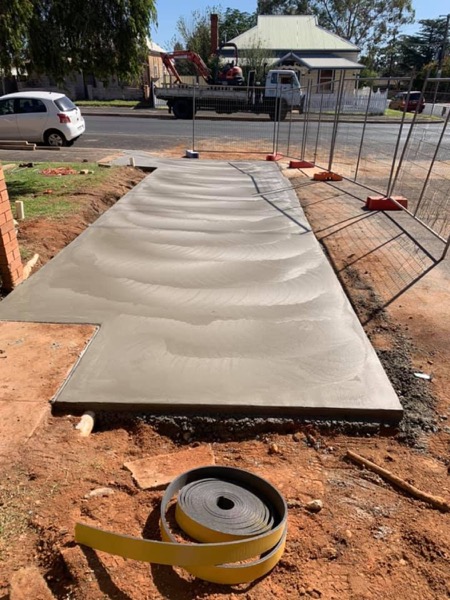 A broom-finished concrete pad sitting on cut red soil behind temporary fencing
