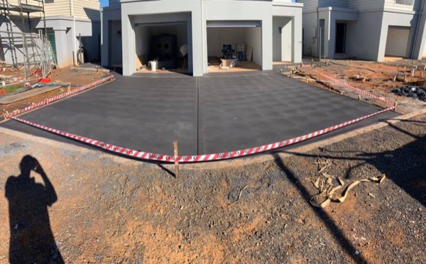 A finished driveway slab in front of a new build behind hazard tape