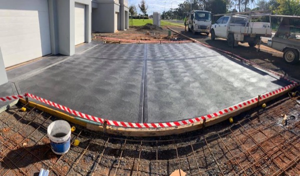 A jointed garage apron behind hazard tape with utes parked on the street