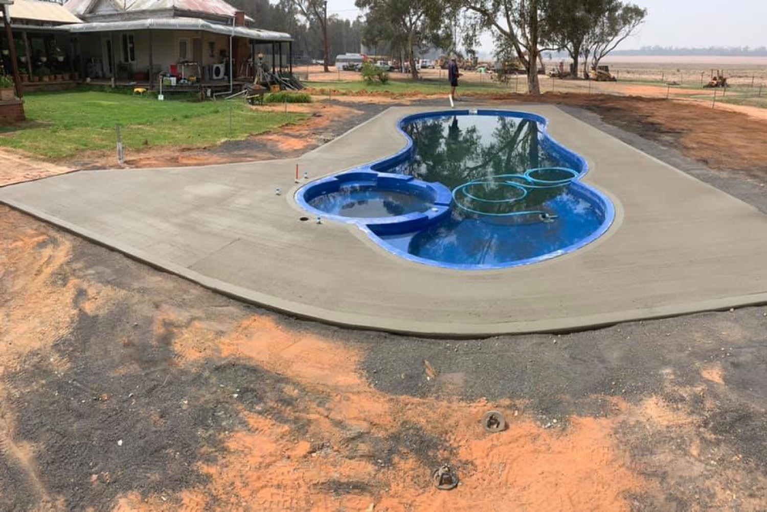 A concrete surround poured around a swimming pool on a rural property